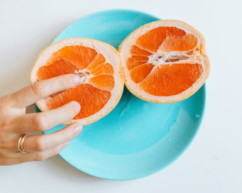 Zwei Hälften einer Orange liegen auf einem blauen Teller. Ein Hand greift eine Hälfte.